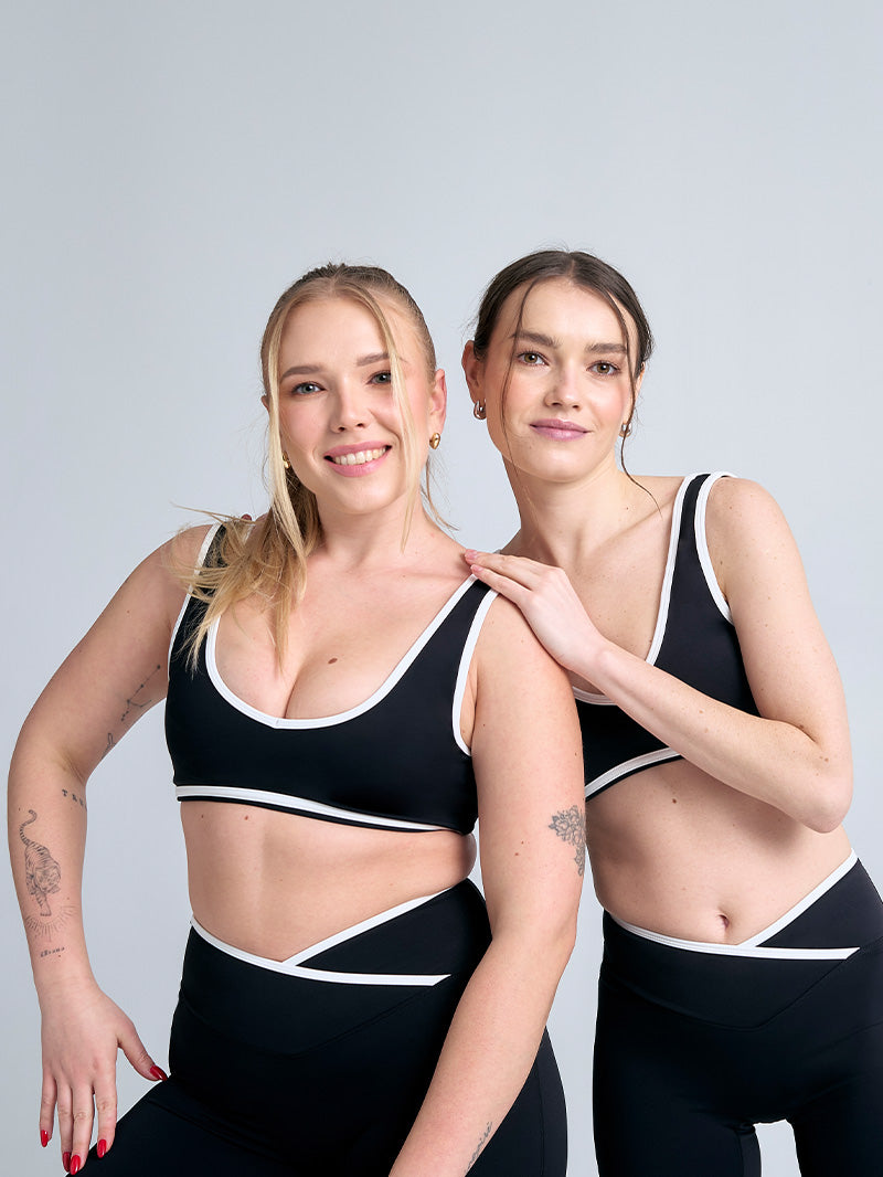 Dwie modelki w czarnych stanikach JOYINME Dual Essence na neutralnym tle. Elastyczny materiał i przemyślana konstrukcja z białymi lamówkami tworzą elegancki duet, idealny zarówno na trening, jak i po nim.