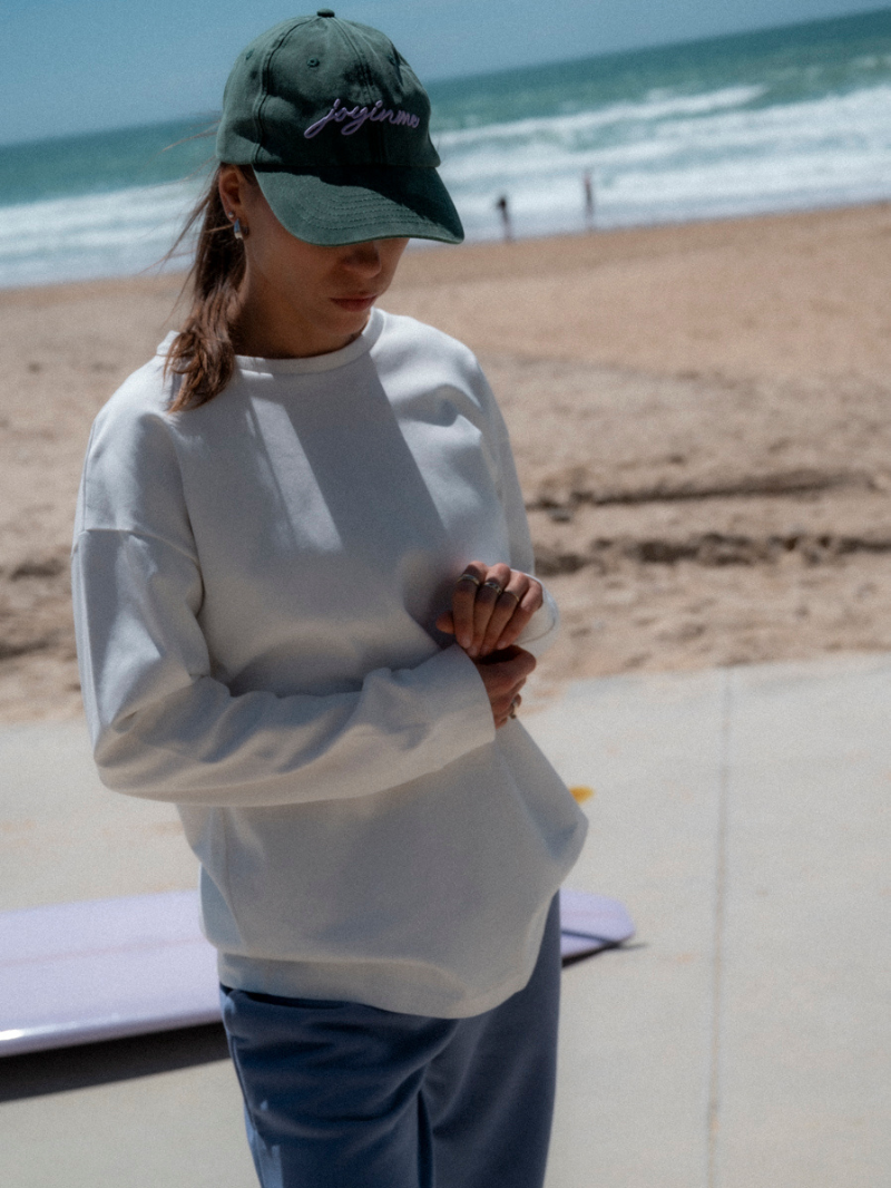 Biała koszulka damska z długimi rękawami o luźnym kroju i z nadrukiem - outfit z szerokimi spodniami i zieloną czapką